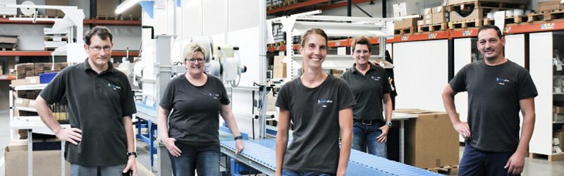 Fünf Mitarbeiter von hydrophon stehen im Betrieb und lächeln in die Kamera.
